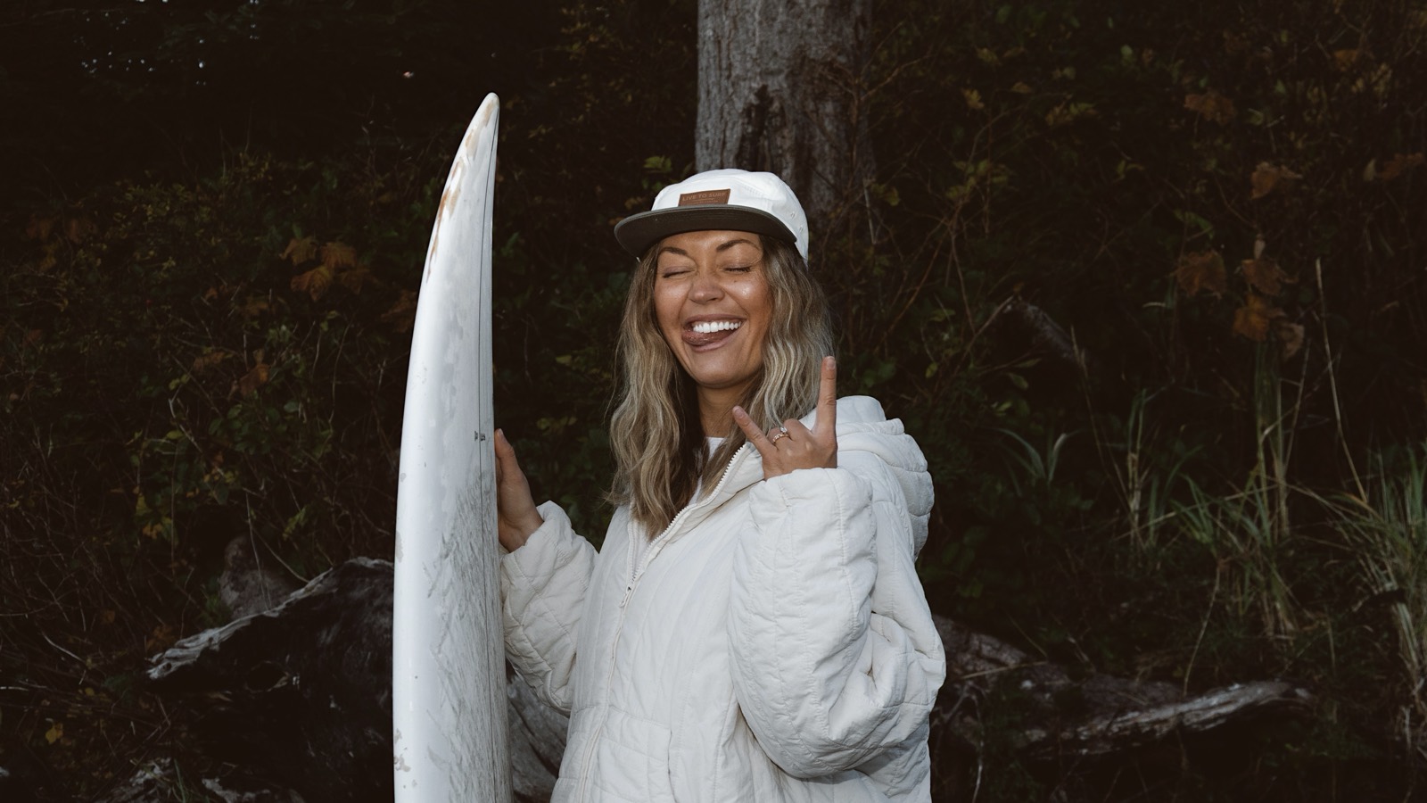 A guest laughing, holding a surfboard against the cedar