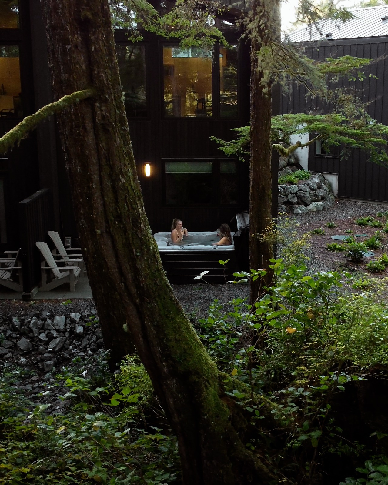 A cabin at dusk, warm light and a hot tub among the trees